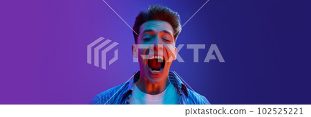 Portrait of young emotive man guy in casual clothes showing success and winning look, excitement against gradient purple background in neon light 102525221
