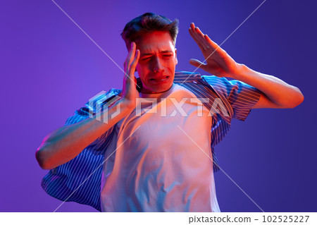 Portrait of young emotional man in casual clothes showing emotions of stress, feeling tired against gradient purple background in neon light Portrait of young emotional man in casual clothes showing emotions of stress, feeling tired against gradient purple background in neon light 102525227