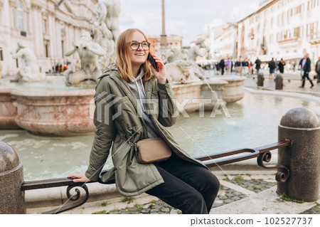 A happy blond woman tourist is standing of the famous Piazza Navona in Rome, Italy. Concept of traveling famous landmarks. Girl with smartphone is walking on a sunny day A happy blond woman tourist is standing of the famous Piazza Navona in Rome, Italy. Concept of traveling famous landmarks. Girl with smartphone is walking on a sunny day 102527737
