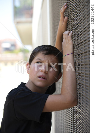 Teen in shorts and black T-shirt leaning on a wall while looking away Teen in shorts and black T-shirt leaning on a wall while looking away 102531448