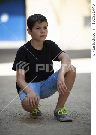 Teen in shorts and black t-shirt crouching while looking at the camera outdoors 102531449