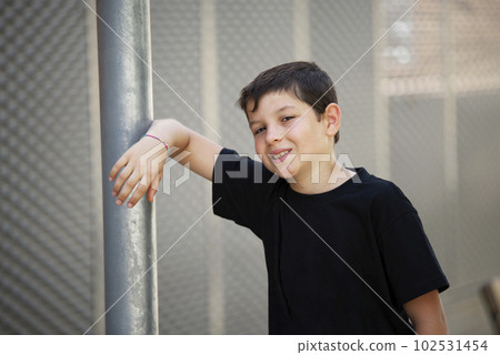 Teen in shorts and black T-shirt leaning on a wall outdoors while looking at camera Teen in shorts and black T-shirt leaning on a wall outdoors while looking at camera 102531454