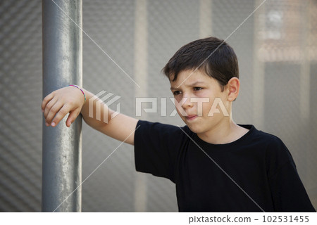 Teen in shorts and black T-shirt leaning on a wall outdoors while looking at camera Teen in shorts and black T-shirt leaning on a wall outdoors while looking at camera 102531455