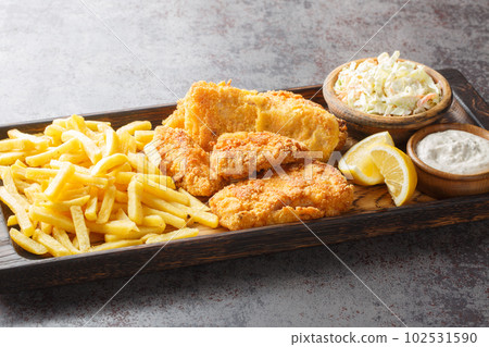 Close up battered fish with coleslaw, French fries, tartar sauce and lemon on the wooden board. Horizontal 102531590