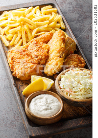 Fast food breaded fried fish served with coleslaw, french fries and tartar sauce on a wooden tray. Vertical Fast food breaded fried fish served with coleslaw, french fries and tartar sauce on a wooden tray. Vertical 102531592