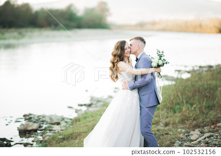 Beautifull wedding couple kissing and embracing near the shore of a mountain river with stones 102532156