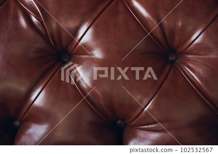 The texture of the background is a close-up of brown genuine leather, upholstered furniture in retro Chesterfield style with a deep diamond pattern and buttons. High quality photo 102532567