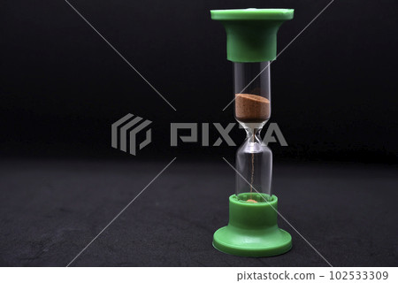 Glass hourglass on a black background. Multicolored glass hourglass. Glass hourglass on a black background. Multicolored glass hourglass. 102533309