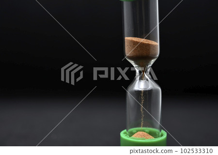 Glass hourglass on a black background. Multicolored glass hourglass. Glass hourglass on a black background. Multicolored glass hourglass. 102533310