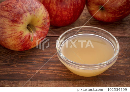 unfiltered, raw apple cider vinegar with mother - a small glass bowl with fresh red apples 102534599