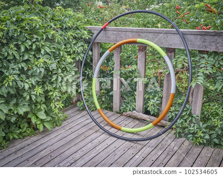 weighted hula hoop and one home made from a sprinkler pipe on a wooden backyard deck in summer scenery, core workout concept weighted hula hoop and one home made from a sprinkler pipe on a wooden backyard deck in summer scenery, core workout concept 102534605