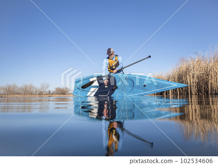 senior male paddler is launching a stand up paddleboard on a calm lake in early spring, frog perspective from an action camera at water level senior male paddler is launching a stand up paddleboard on a calm lake in early spring, frog perspective from an action camera at water level 102534606