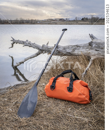 waterproof duffel and stand up paddle on a lake shore waterproof duffel and stand up paddle on a lake shore 102534613