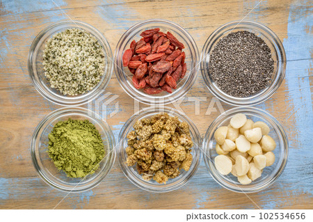 superfood abstract - hemp seeds, goji berries, chia seeds, matcha tea powder, mulberries and macadamia nuts - top view of glass bowls on wood superfood abstract - hemp seeds, goji berries, chia seeds, matcha tea powder, mulberries and macadamia nuts - top view of glass bowls on wood 102534656