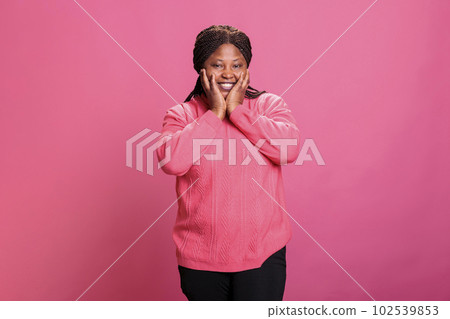 African american model smiling in front of camera, posing with positive joyful expressions. Young cheerful woman feeling excited and happy, enjoying good times standing over pink background. 102539853