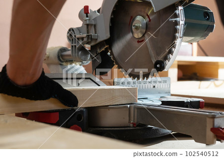 The master cuts the board with a circular saw in the workshop. Close-up of a carpenter's male hands at work. 102540512