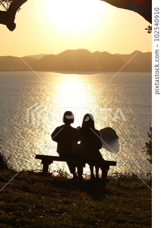Two women on a bench with a view of the mountains and the sea, women's silhouettes, sunset Two women on a bench with a view of the mountains and the sea, women's silhouettes, sunset 102540910