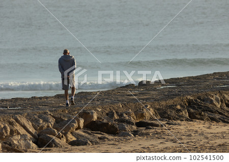 A lonely elderly man walks on a rocky ledge by the sea A lonely elderly man walks on a rocky ledge by the sea 102541500