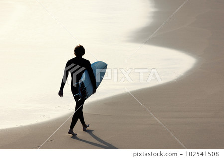 Black silhouette of a man with a surfboard walking on the beach Black silhouette of a man with a surfboard walking on the beach 102541508