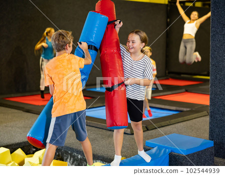 Cheerful school-age boy and girl friends having fun on inflatable gladiator fight arena in indoor amusement center Cheerful school-age boy and girl friends having fun on inflatable gladiator fight arena in indoor amusement center 102544939