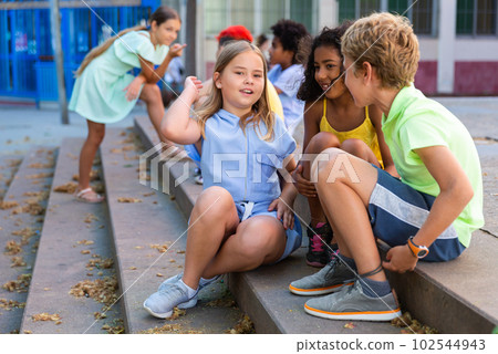 Happy tweenagers friends sitting on steps outdoors and chatting 102544943