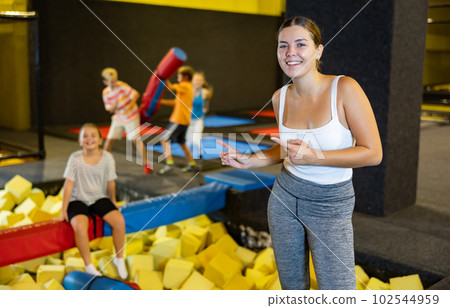 Portrait of cheerful young female in sportswear posing and smiling at camera behind foam cube pit at trampolines center Portrait of cheerful young female in sportswear posing and smiling at camera behind foam cube pit at trampolines center 102544959