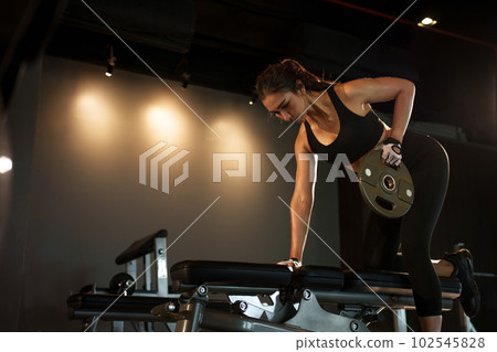 Sporty woman exercising with weight plate in the gym. Sporty woman exercising with weight plate in the gym. 102545828