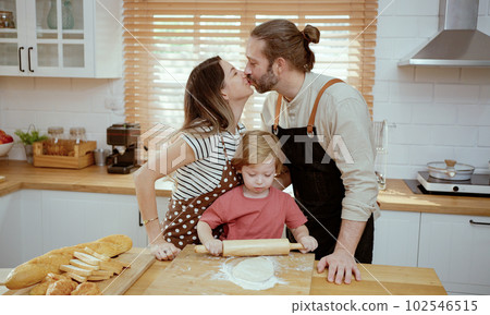 Father and mother teaching baby son kneading dough on kitchen counter at home. Parents and boy kid enjoy and fun indoors activity cooking together. 102546515