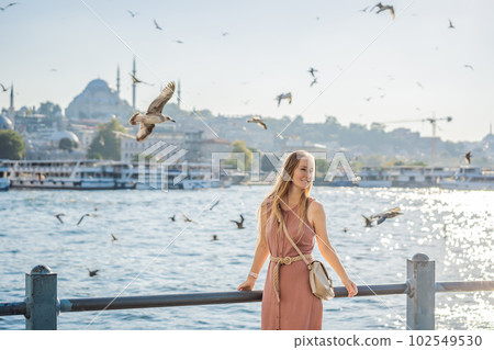Young woman traveler in pinc dress enjoying great view of the Bosphorus and lots of seagulls in Istanbul 102549530
