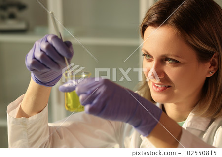 Smiling female scientist holding flask with yellow liquid 102550815