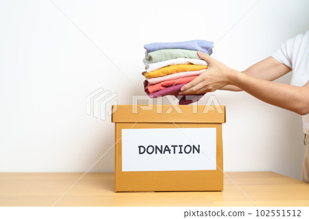 Donation, Charity, Volunteer, Giving and Delivery Concept. Hand holding Clothes into Donation box at home or office for support and help poor, refugee and homeless people. Copy space for text Donation, Charity, Volunteer, Giving and Delivery Concept. Hand holding Clothes into Donation box at home or office for support and help poor, refugee and homeless people. Copy space for text 102551512