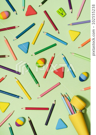 Open Yellow pencil case with Colored Pencils and rubber erasers background pattern on light green. Back to School or drawing and creativity concept. Copy space in center. Top view 102555238