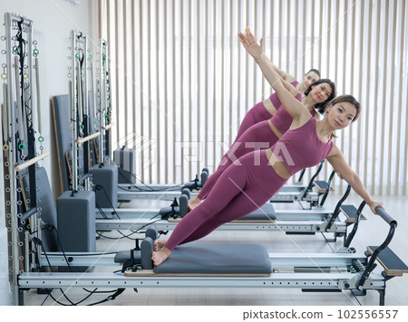 Three Asian women in pink sportswear doing side planks on a reformer. Pilates classes. Three Asian women in pink sportswear doing side planks on a reformer. Pilates classes. 102556557