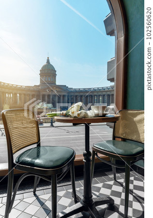 Cappuccino, delicious whipped creme dessert and white calla flowers on wooden table in cafe with beautiful view on Kazan Cathedral in Saint Petersburg. Love and romance concept. 102560620