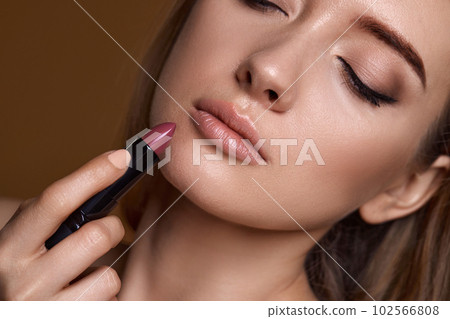 beautiful young smiling woman holding nude pink lipstick 102566808