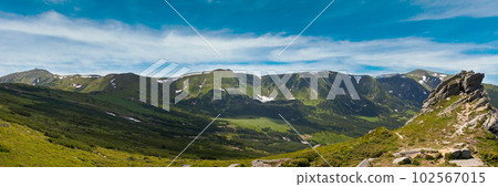 Summer mountain view with snow and big stones on mountainside. 102567015