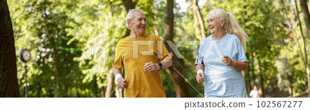 Positive senior family couple run tgether along road in park 102567277