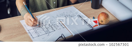 Close up shot of hand of female interior designer making notes on a blueprint, sitting at the table in her office 102567301