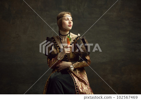 Portrait of young girl, princess, royal person in vintage dress posing with carrot against dark green background. 102567469
