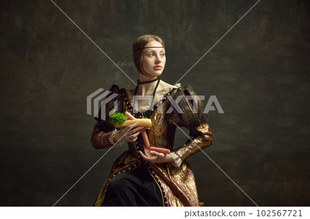 Portrait of young beautiful woman in vintage, elegant dress holding giant hot dog against dark green background. Fast food Portrait of young beautiful woman in vintage, elegant dress holding giant hot dog against dark green background. Fast food 102567721