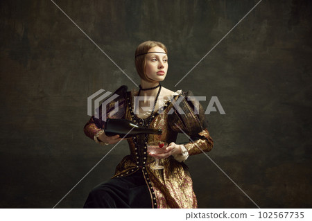 Portrait of young girl, princess in vintage dress pouring champagne into glass against dark green background. Party, celebration Portrait of young girl, princess in vintage dress pouring champagne into glass against dark green background. Party, celebration 102567735