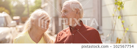 Positive senior family couple with cups walks together along street 102567754