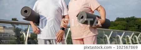 Mature couple in sportswear with mats ready for workout on footbridge at sunset closeup 102567869