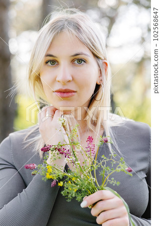 Spring lifestyle portrait of beautiful young woman smiling and holding bouquet of wild flowers. Happiness and love concept 102568647