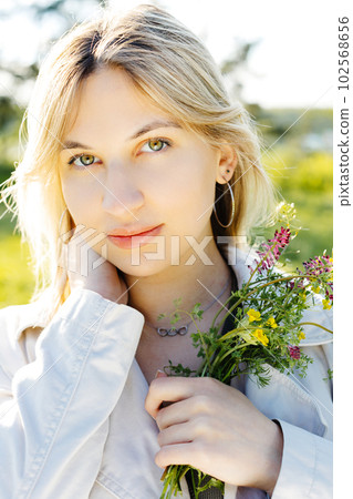 Spring lifestyle portrait of beautiful young woman smiling and holding bouquet of wild flowers. Happiness and love concept 102568656