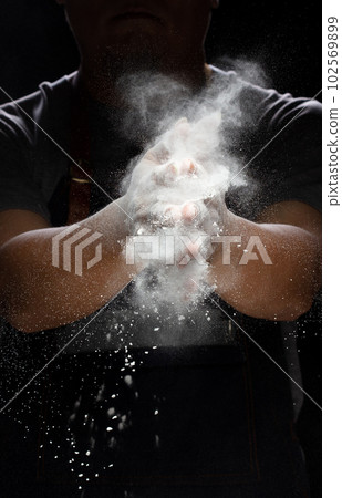 Chef prepare white flour dust for cooking bakery food. Elderly man Chef clap hand, white flour dust explode fly in air. Flour stop motion in air with freeze high speed shutter, black background Chef prepare white flour dust for cooking bakery food. Elderly man Chef clap hand, white flour dust explode fly in air. Flour stop motion in air with freeze high speed shutter, black background 102569899