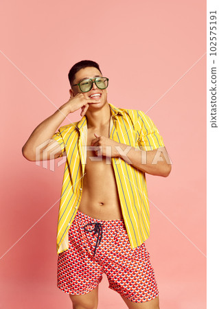 Portrait of handsome young guy, student wearing summer clothes and tanned skin smiling over pink studio background. Bachelor 102575191