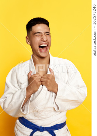 Close up portrait with winner, male taekwondo, karate athlete wearing white kimono relaxing after fight over yellow background 102575240