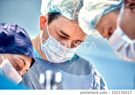 Close-up view of surgeons faces in medical masks during a complex and intense operation, doctors save the patient's life, teamwork of surgeons Close-up view of surgeons faces in medical masks during a complex and intense operation, doctors save the patient's life, teamwork of surgeons 102576817