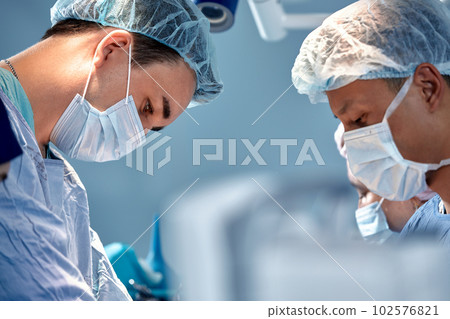 Close-up view of surgeons faces in medical masks during a complex and intense operation, doctors save the patient's life, teamwork of surgeons 102576821